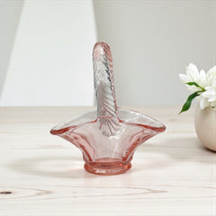 Vintage pink Depression glass favor basket with ruffled rim and twisted handle, styled on a neutral surface with soft natural light.
