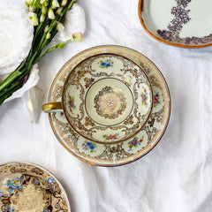 Vintage Tirschenreuth Bavaria demi-tasse and saucer set in cream porcelain with ornate floral clusters and gold scrollwork; footed teacup with gilded handle and rim, saucer marked with crown and shield logo and red glaze number 2284.
