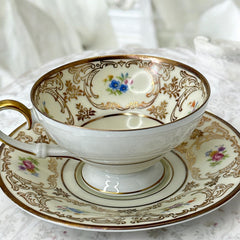 Vintage Tirschenreuth Bavaria demi-tasse and saucer set in cream porcelain with ornate floral clusters and gold scrollwork; footed teacup with gilded handle and rim, saucer marked with crown and shield logo and red glaze number 2284.