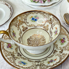 Vintage Tirschenreuth Bavaria demi-tasse and saucer set in cream porcelain with ornate floral clusters and gold scrollwork; footed teacup with gilded handle and rim, saucer marked with crown and shield logo and red glaze number 2284.