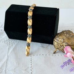 Vintage 1960s Trifari Crown sapphire blue rhinestone birthstone bracelet with brushed gold tone ribbon links and fold‑over clasp.