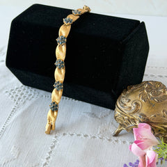 Vintage 1960s Trifari Crown sapphire blue rhinestone birthstone bracelet with brushed gold tone ribbon links and fold‑over clasp.
