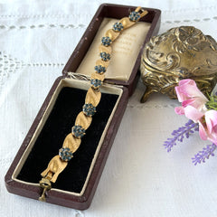 Vintage 1960s Trifari Crown sapphire blue rhinestone birthstone bracelet with brushed gold tone ribbon links and fold‑over clasp.