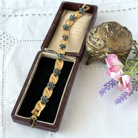 Vintage 1960s Trifari Crown sapphire blue rhinestone birthstone bracelet with brushed gold tone ribbon links and fold‑over clasp.