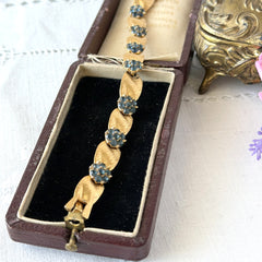 Vintage 1960s Trifari Crown sapphire blue rhinestone birthstone bracelet with brushed gold tone ribbon links and fold‑over clasp.
