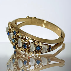 Vintage Trifari “Clair de Lune” bracelet by Alfred Philippe, gold-plated hinged bangle with crescent-shaped opalized faux moonstones, sapphire blue and clear rhinestones, shown in various lighting and angles to highlight design and craftsmanship
