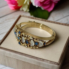 Vintage Trifari “Clair de Lune” bracelet by Alfred Philippe, gold-plated hinged bangle with crescent-shaped opalized faux moonstones, sapphire blue and clear rhinestones, shown in various lighting and angles to highlight design and craftsmanship