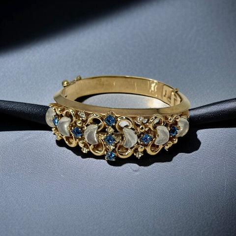 Vintage Trifari “Clair de Lune” bracelet by Alfred Philippe, gold-plated hinged bangle with crescent-shaped opalized faux moonstones, sapphire blue and clear rhinestones, shown in various lighting and angles to highlight design and craftsmanship