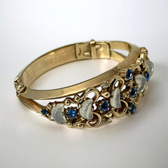 Vintage Trifari “Clair de Lune” bracelet by Alfred Philippe, gold-plated hinged bangle with crescent-shaped opalized faux moonstones, sapphire blue and clear rhinestones, shown in various lighting and angles to highlight design and craftsmanship