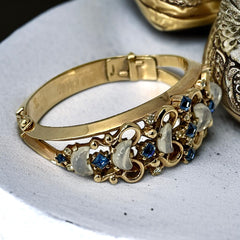 Vintage Trifari “Clair de Lune” bracelet by Alfred Philippe, gold-plated hinged bangle with crescent-shaped opalized faux moonstones, sapphire blue and clear rhinestones, shown in various lighting and angles to highlight design and craftsmanship