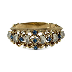 Vintage Trifari “Clair de Lune” bracelet by Alfred Philippe, gold-plated hinged bangle with crescent-shaped opalized faux moonstones, sapphire blue and clear rhinestones, shown in various lighting and angles to highlight design and craftsmanship