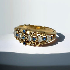 Vintage Trifari “Clair de Lune” bracelet by Alfred Philippe, gold-plated hinged bangle with crescent-shaped opalized faux moonstones, sapphire blue and clear rhinestones, shown in various lighting and angles to highlight design and craftsmanship