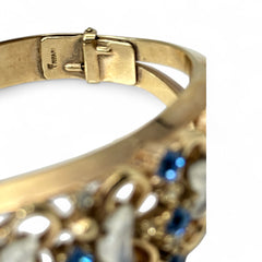 Vintage Trifari “Clair de Lune” bracelet by Alfred Philippe, gold-plated hinged bangle with crescent-shaped opalized faux moonstones, sapphire blue and clear rhinestones, shown in various lighting and angles to highlight design and craftsmanship