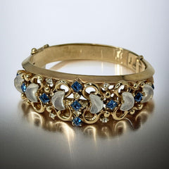 Vintage Trifari “Clair de Lune” bracelet by Alfred Philippe, gold-plated hinged bangle with crescent-shaped opalized faux moonstones, sapphire blue and clear rhinestones, shown in various lighting and angles to highlight design and craftsmanship