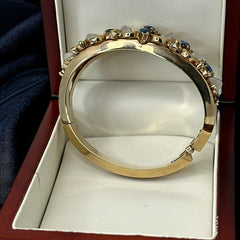 Vintage Trifari “Clair de Lune” bracelet by Alfred Philippe, gold-plated hinged bangle with crescent-shaped opalized faux moonstones, sapphire blue and clear rhinestones, shown in various lighting and angles to highlight design and craftsmanship