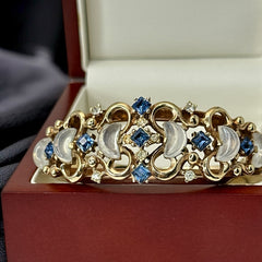 Vintage Trifari “Clair de Lune” bracelet by Alfred Philippe, gold-plated hinged bangle with crescent-shaped opalized faux moonstones, sapphire blue and clear rhinestones, shown in various lighting and angles to highlight design and craftsmanship