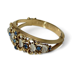 Vintage Trifari “Clair de Lune” bracelet by Alfred Philippe, gold-plated hinged bangle with crescent-shaped opalized faux moonstones, sapphire blue and clear rhinestones, shown in various lighting and angles to highlight design and craftsmanship