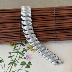 Vintage Trifari Crown silver‑tone bracelet with sculptural brushed and polished links, photographed on botanical paper and wood background.