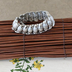Vintage Trifari Crown silver‑tone bracelet with sculptural brushed and polished links, photographed on botanical paper and wood background.
