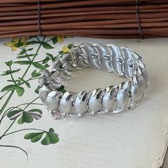 Vintage Trifari Crown silver‑tone bracelet with sculptural brushed and polished links, photographed on botanical paper and wood background.