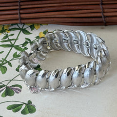 Vintage Trifari Crown silver‑tone bracelet with sculptural brushed and polished links, photographed on botanical paper and wood background.