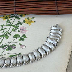 Vintage Trifari Crown silver‑tone bracelet with sculptural brushed and polished links, photographed on botanical paper and wood background.