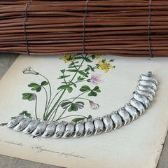 Vintage Trifari Crown silver‑tone bracelet with sculptural brushed and polished links, photographed on botanical paper and wood background.