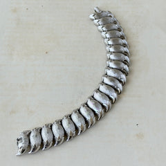 Vintage Trifari Crown silver‑tone bracelet with sculptural brushed and polished links, photographed on botanical paper and wood background.