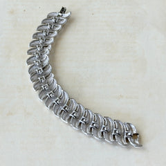 Vintage Trifari Crown silver‑tone bracelet with sculptural brushed and polished links, photographed on botanical paper and wood background.