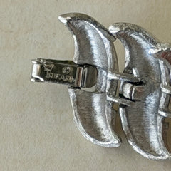 Vintage Trifari Crown silver‑tone bracelet with sculptural brushed and polished links, photographed on botanical paper and wood background.