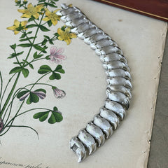 Vintage Trifari Crown silver‑tone bracelet with sculptural brushed and polished links, photographed on botanical paper and wood background.