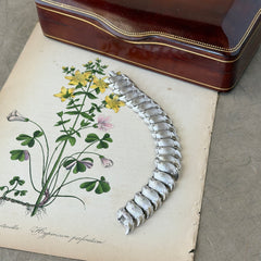 Vintage Trifari Crown silver‑tone bracelet with sculptural brushed and polished links, photographed on botanical paper and wood background.
