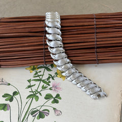 Vintage Trifari Crown silver‑tone bracelet with sculptural brushed and polished links, photographed on botanical paper and wood background.