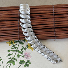 Vintage Trifari Crown silver‑tone bracelet with sculptural brushed and polished links, photographed on botanical paper and wood background.