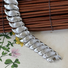 Vintage Trifari Crown silver‑tone bracelet with sculptural brushed and polished links, photographed on botanical paper and wood background.