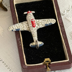 Vintage Trifari airplane brooch with clear stones, red nose detail, and blue enamel accents.