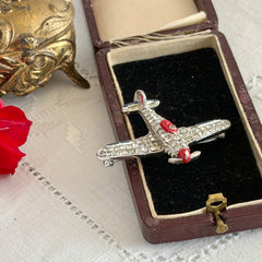 Vintage Trifari airplane brooch with clear stones, red nose detail, and blue enamel accents.