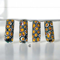 A set of vintage Venetian millefiori African trade beads in vibrant green and yellow. The tube-shaped glass beads, originating from Ghana, feature intricate floral patterns and showcase the rich history of 19th and 20th-century trade. Some beads show minor chips due to age, adding to their authentic vintage charm.