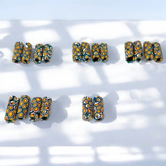 A set of vintage Venetian millefiori African trade beads in vibrant green and yellow. The tube-shaped glass beads, originating from Ghana, feature intricate floral patterns and showcase the rich history of 19th and 20th-century trade. Some beads show minor chips due to age, adding to their authentic vintage charm.