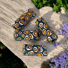 A set of vintage Venetian millefiori African trade beads in vibrant green and yellow. The tube-shaped glass beads, originating from Ghana, feature intricate floral patterns and showcase the rich history of 19th and 20th-century trade. Some beads show minor chips due to age, adding to their authentic vintage charm