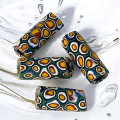 A set of vintage Venetian millefiori African trade beads in vibrant green and yellow. The tube-shaped glass beads, originating from Ghana, feature intricate floral patterns and showcase the rich history of 19th and 20th-century trade. Some beads show minor chips due to age, adding to their authentic vintage charm