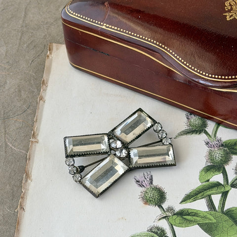 Vintage Victorian silver‑tone bow brooch with emerald‑cut clear glass stones and paste rhinestones, shown from multiple angles highlighting its antique patina and craftsmanship.