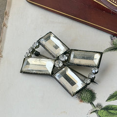 Vintage Victorian silver‑tone bow brooch with emerald‑cut clear glass stones and paste rhinestones, shown from multiple angles highlighting its antique patina and craftsmanship.
