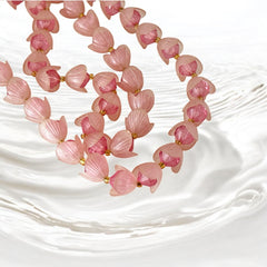 Vintage 1950s West Germany double-strand necklace displayed on black velvet stand, featuring frosted pink plastic petal beads encasing darker pink faceted centers, finished with a round pink cabochon clasp.