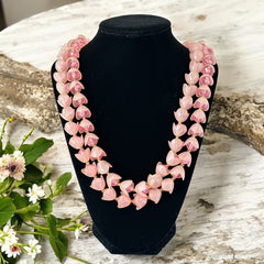 Vintage 1950s West Germany double-strand necklace displayed on black velvet stand, featuring frosted pink plastic petal beads encasing darker pink faceted centers, finished with a round pink cabochon clasp.