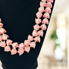 Vintage 1950s West Germany double-strand necklace displayed on black velvet stand, featuring frosted pink plastic petal beads encasing darker pink faceted centers, finished with a round pink cabochon clasp.