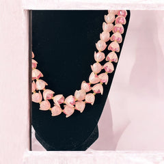 Vintage 1950s West Germany double-strand necklace displayed on black velvet stand, featuring frosted pink plastic petal beads encasing darker pink faceted centers, finished with a round pink cabochon clasp.