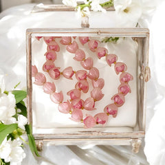 Vintage 1950s West Germany double-strand necklace displayed on black velvet stand, featuring frosted pink plastic petal beads encasing darker pink faceted centers, finished with a round pink cabochon clasp.