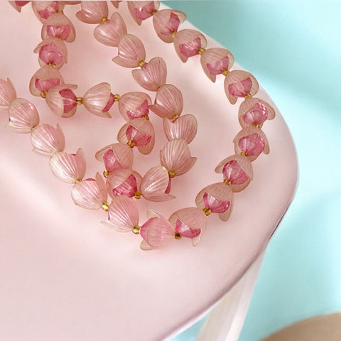 Vintage 1950s West Germany double-strand necklace displayed on black velvet stand, featuring frosted pink plastic petal beads encasing darker pink faceted centers, finished with a round pink cabochon clasp.
