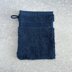 Solid navy cotton terry pocket washcloth with ribbed cuff and hanging loop, shown on a speckled surface.